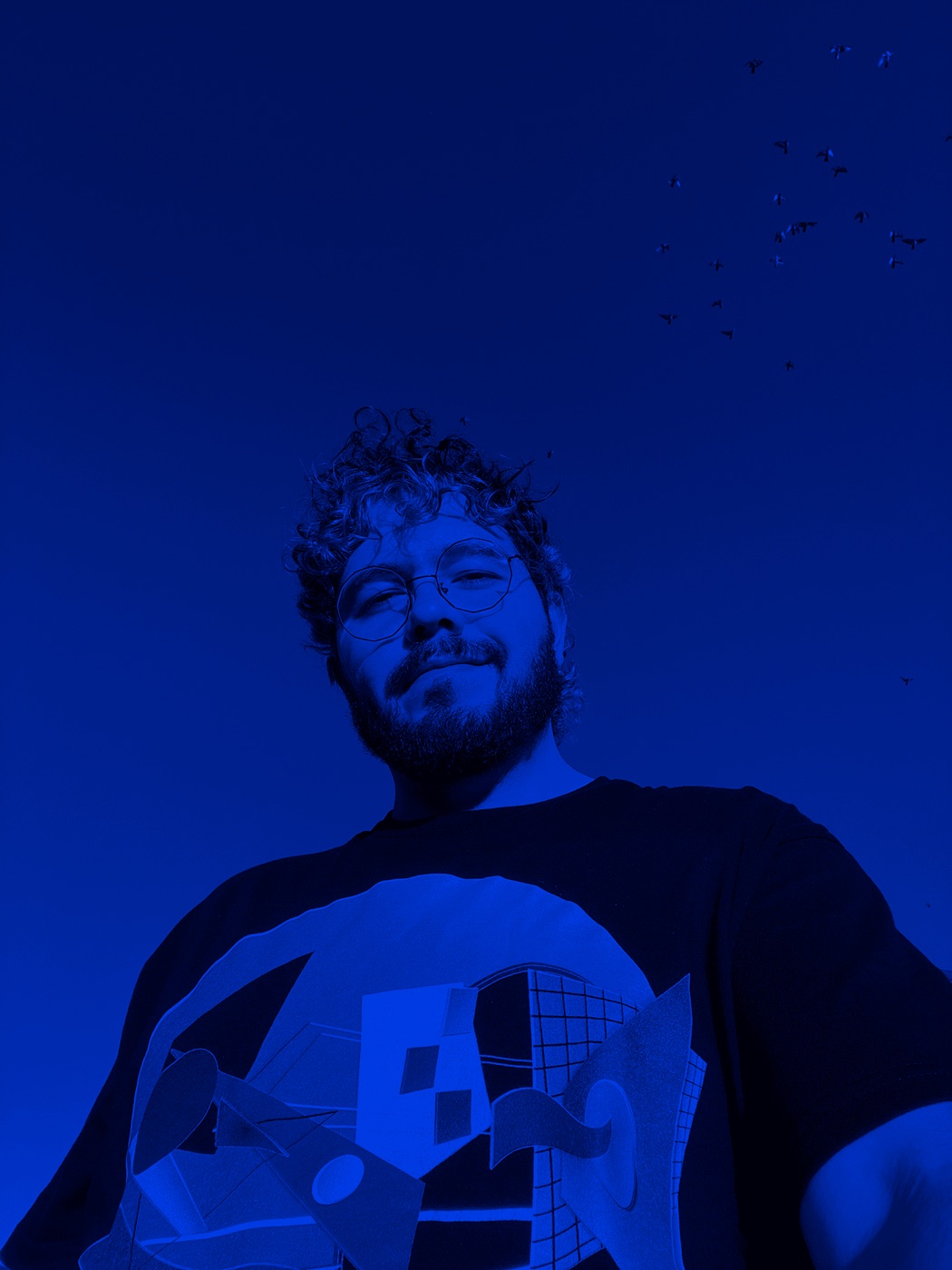 Juan, smiling, photographed from below against a deep blue sky with birds overhead