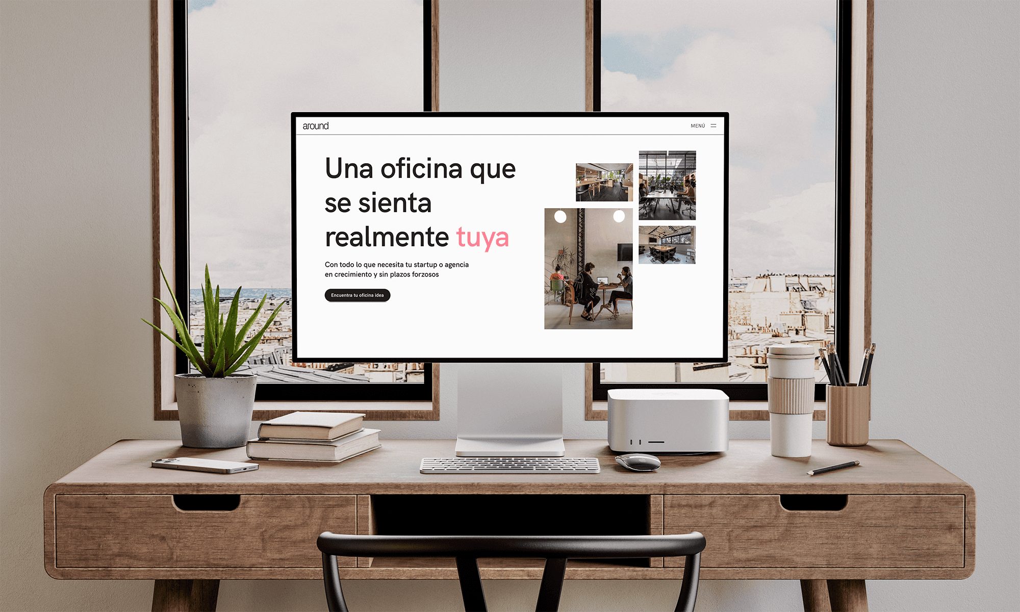 La página de inicio de Around en un monitor, sobre un escritorio de madera junto a una ventana